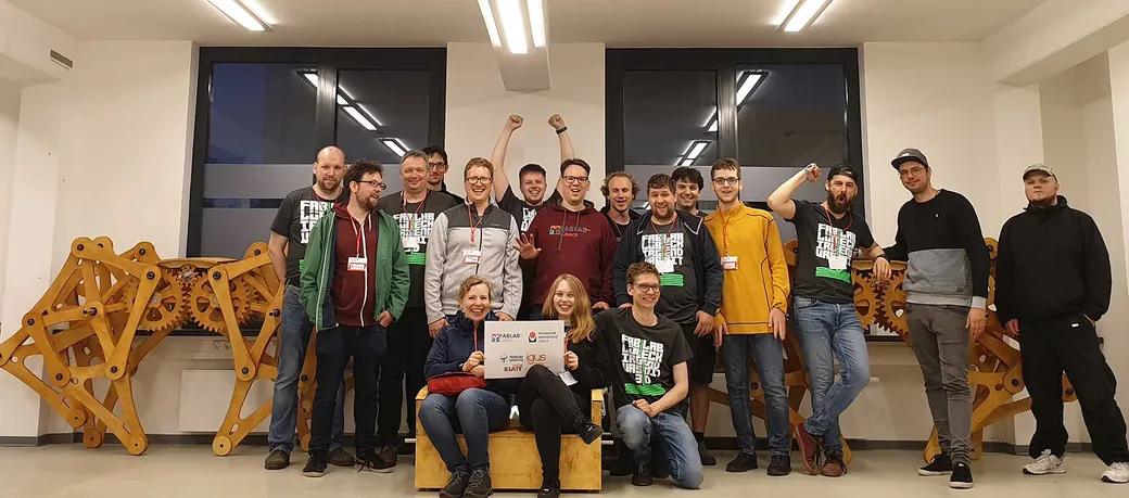 Gruppenbild der FabLab-Community vor großen Holzmodellen mit Zahnrädern